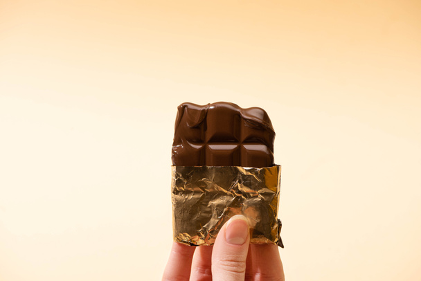 vista ritagliata della donna che tiene deliziosa barretta di cioccolato al latte in lamina d'oro isolata sul beige
 - Foto, immagini