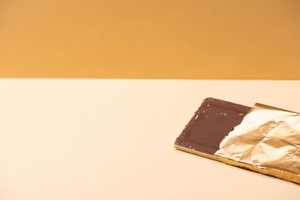delicious milk chocolate bar in golden foil on beige background - Foto, afbeelding