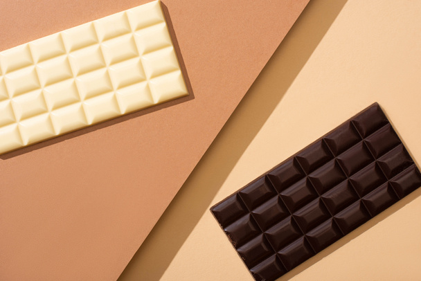 top view of delicious whole white and dark chocolate bars on beige background - Foto, afbeelding