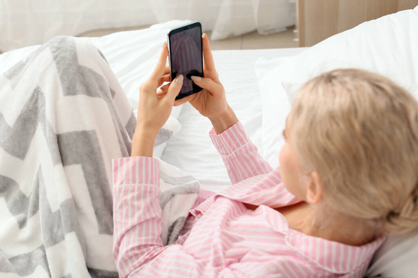Young woman with mobile phone in bedroom - Photo, image