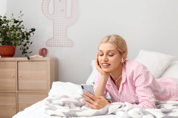 Mujer joven con teléfono móvil escuchando música en el dormitorio
 - Foto, imagen