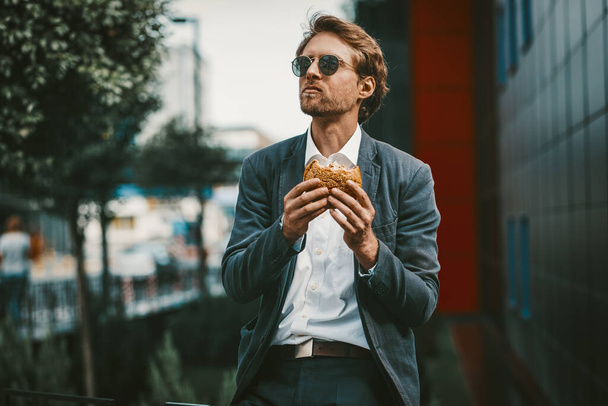 Young hungry trainee having a burger on a lunch break - 写真・画像