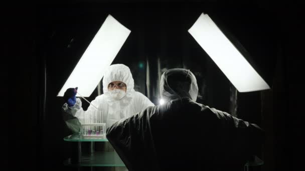 Dois cientistas trabalham no laboratório em fatos de protecção.
 - Filmagem, Vídeo