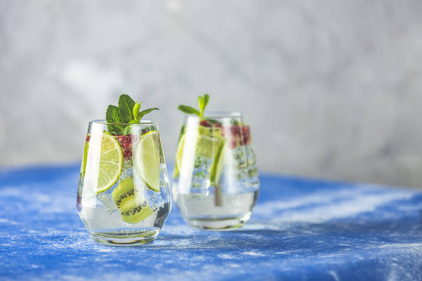 Detox water or martini tonic cocktail with kiwi, lime and ice, decoration pomegranate and mint. Summer fresh lime soda cocktail, selective focus. - Foto, imagen