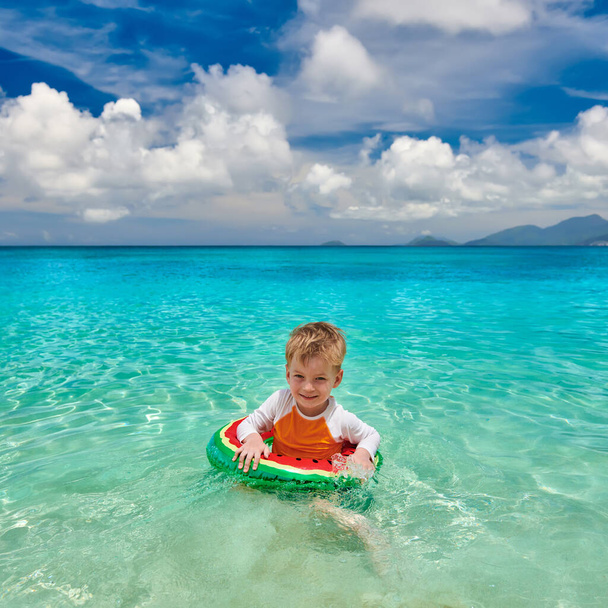 Трехлетний мальчик на пляже в Сейшельских островах плавает с надувным кольцом
 - Фото, изображение