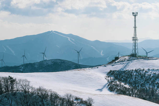 Electric Turbine Windmill on a snowy ground. Winter hill landscape with blue sky. - Photo, Image