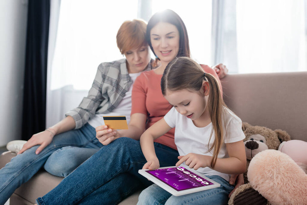 Kind nutzt digitales Tablet mit E-Health-App am Bildschirm in der Nähe von Müttern mit Kreditkarte und Plüschtieren  - Foto, Bild