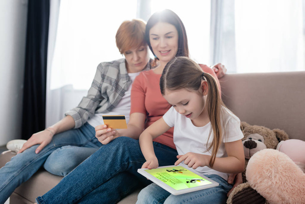 Poika käyttää digitaalista tablettia, jossa on paras ostossovellus ruudulla lähellä äidit luottokortilla kotona
 - Valokuva, kuva