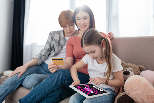 Kronometre uygulamalı dijital tablet kullanan bir çocuk annesinin yanında oturma odasındaki koltukta kredi kartıyla oturuyor. - Fotoğraf, Görsel