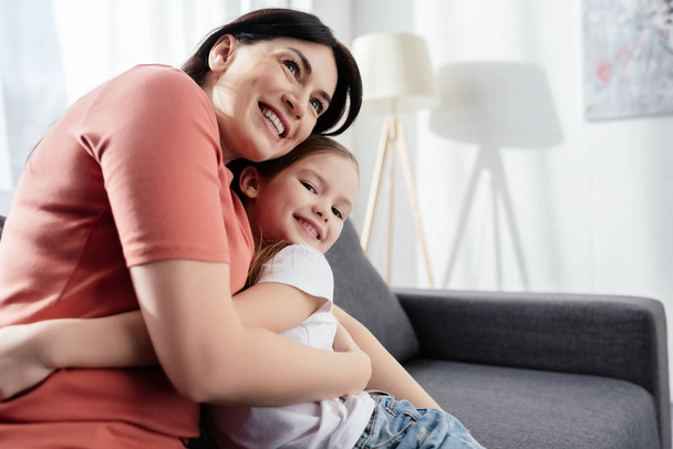 Smiling woman embracing happy daughter on couch  - Photo, Image