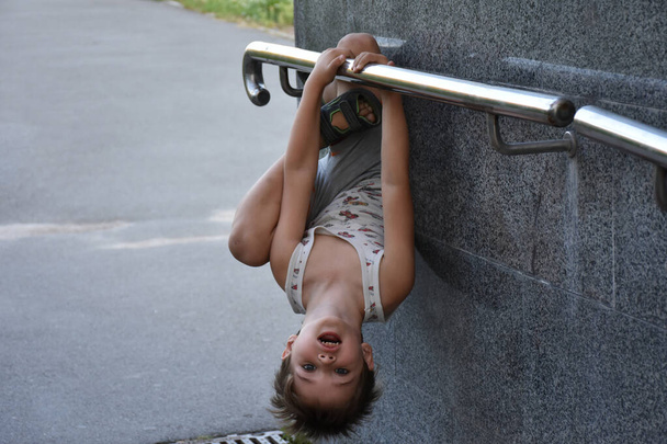 the child hangs upside down on the horizontal bar - Photo, Image