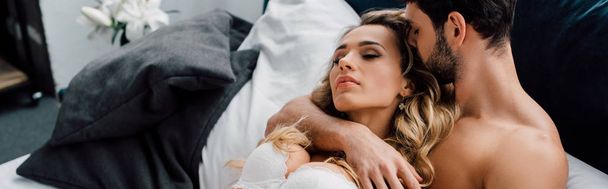 Yakışıklı adamın yatakta seksi kız arkadaşını kucakladığı panoramik bir fotoğraf.  - Fotoğraf, Görsel