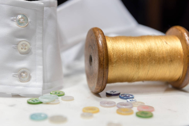 Wooden Spool with Yellow Thread with Assorted Buttons and White Shirt Cuff - Photo, Image