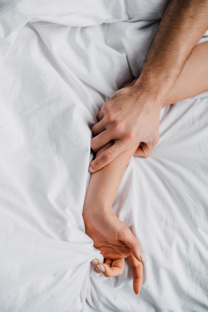 Top view of man holding hand of girlfriend on bed  - Foto, Bild
