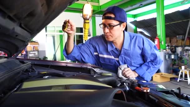 Mécanicien masculin asiatique, portant une lampe pour allumer le moteur pour trouver la cause et fixer le moteur dans le garage Service de réparation
. - Séquence, vidéo