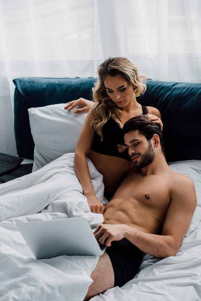 Muscular man looking at laptop near attractive woman on bed  - Fotoğraf, Görsel
