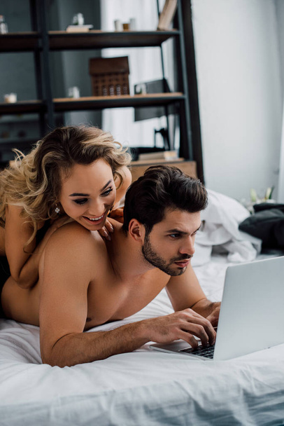 Sorrindo mulher deitada no namorado bonito usando laptop na cama
  - Foto, Imagem