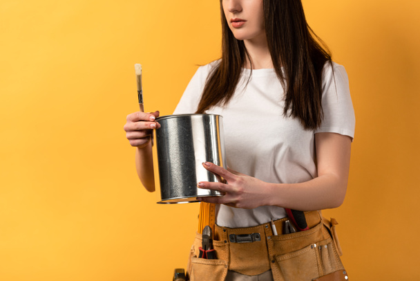 cropped view of handywoman holding paint can and paint brush on yellow background  - Фото, изображение