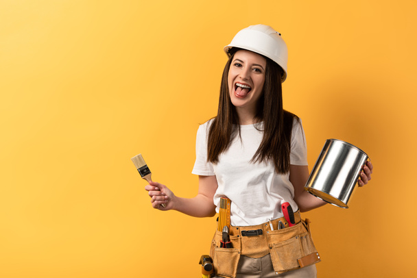 smiling handywoman holding paint brush and paint can on yellow background  - Photo, Image