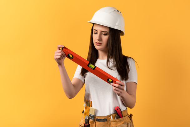 concentrated handywoman  holding spirit level on yellow background  - Photo, Image
