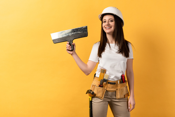 Lächelnde Handarbeiterin im Helm mit Kelle auf gelbem Hintergrund  - Foto, Bild