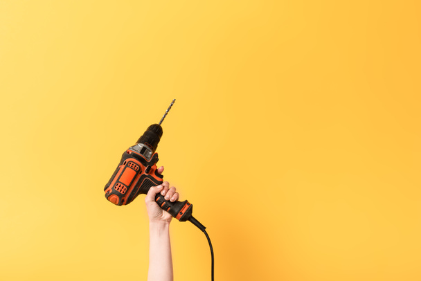 cropped view of woman holding drill on yellow background  - Valokuva, kuva