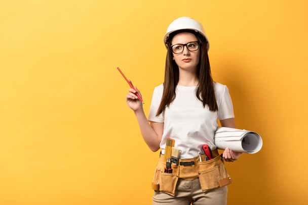 thoughtful handywoman holding blueprint and pencil on yellow background  - Foto, Imagem