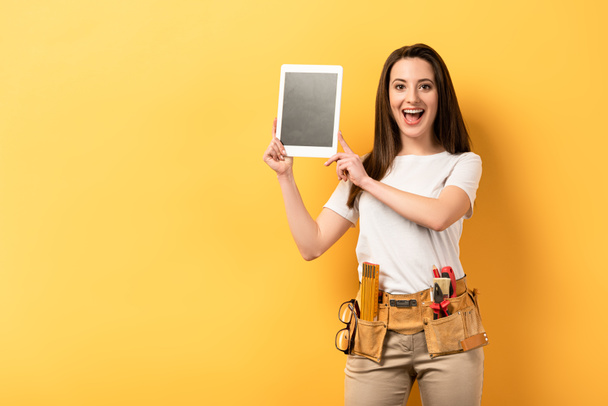 shocked handywoman holding digital tablet with copy space on yellow background  - Fotoğraf, Görsel