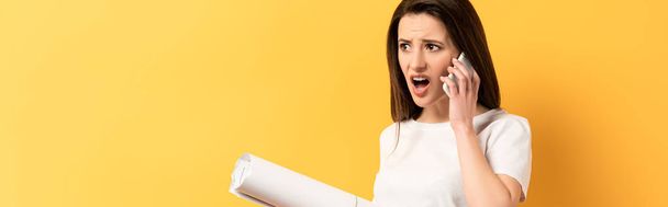 panoramic shot of shocked woman talking on smartphone and holding project on yellow background  - Photo, Image