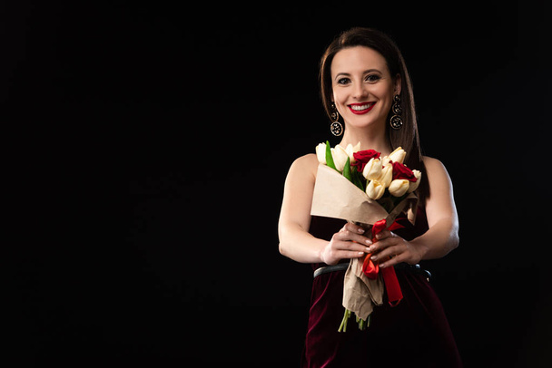 smiling woman in dress holding bouquet isolated on black - Zdjęcie, obraz