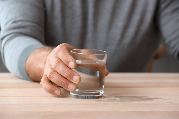 Старший чоловік з синдромом Паркінсона п'є воду вдома, крупним планом
 - Фото, зображення