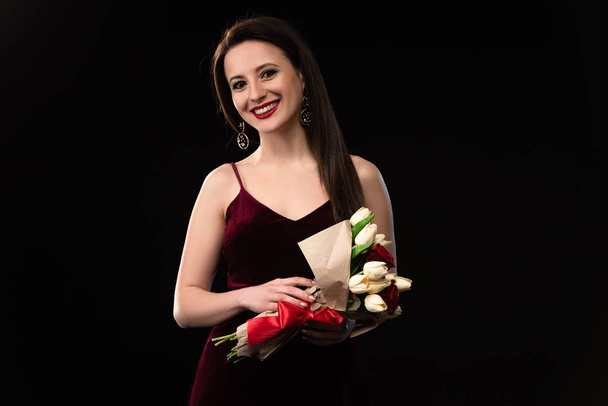 smiling woman in dress holding bouquet isolated on black - Фото, зображення