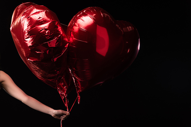 bijgesneden beeld van vrouw met hartvormige ballonnen in 14 februari geïsoleerd op zwart - Foto, afbeelding