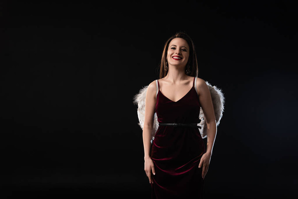 smiling woman in dress with wings looking at camera isolated on black - Foto, immagini