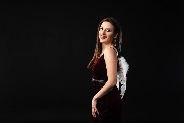 smiling woman in dress with wings looking at camera isolated on black - Foto, immagini