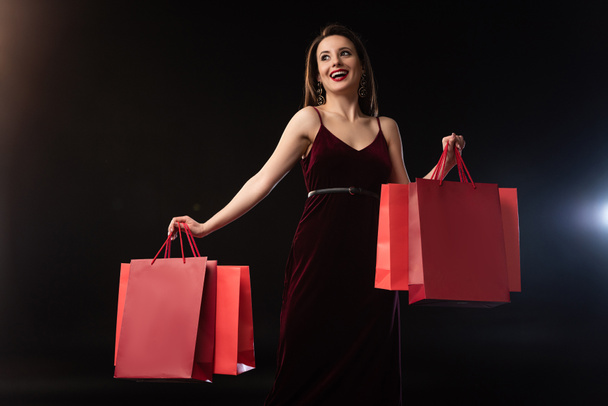 smiling woman in dress holding shopping bags on black background  - Fotó, kép