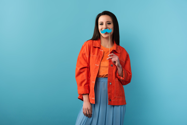 smiling woman holding stick with paper mustache on blue background  - Foto, Bild