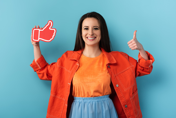 smiling woman showing thumb up and holding paper like on blue background  - Photo, Image