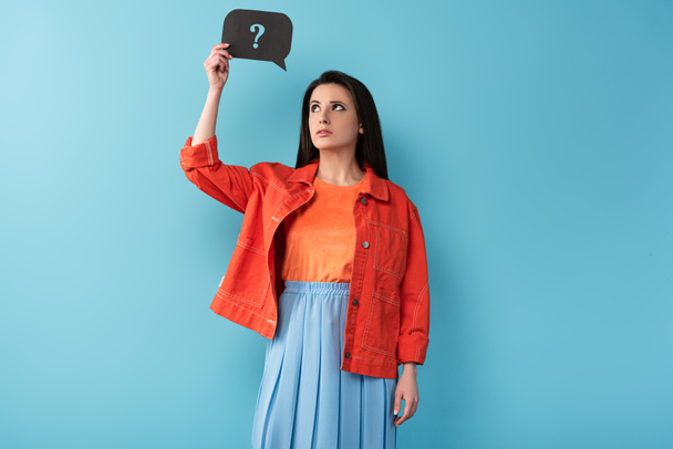 nachdenkliche Frau hält Sprechblase mit Fragezeichen auf blauem Hintergrund  - Foto, Bild