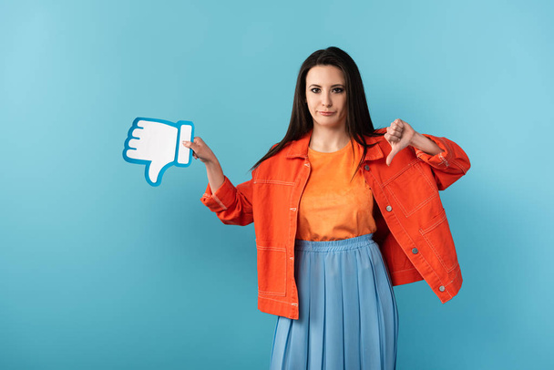 disappointed woman showing thumb down and holding paper dislike on blue background  - Photo, Image