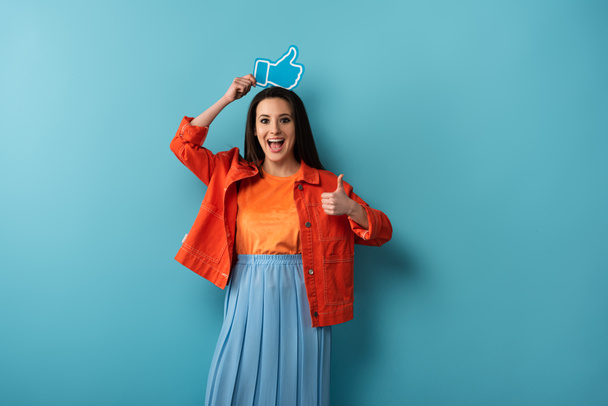 smiling woman showing thumb up and holding paper like on blue background  - Foto, Bild