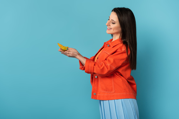 widok z boku uśmiechnięta kobieta gospodarstwa papieru motyl na niebieskim tle  - Zdjęcie, obraz