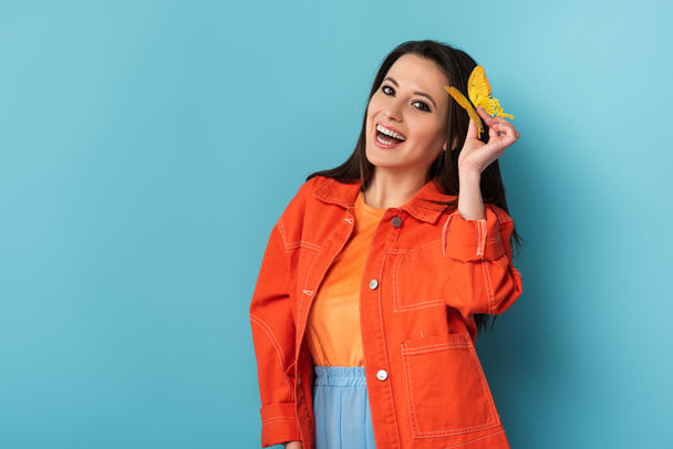 smiling woman holding paper butterfly on blue background  - Foto, imagen