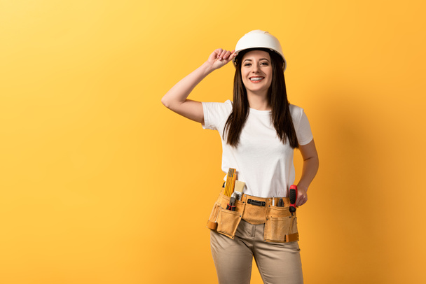 smiling handywoman in helmet looking at camera on yellow background  - Photo, Image