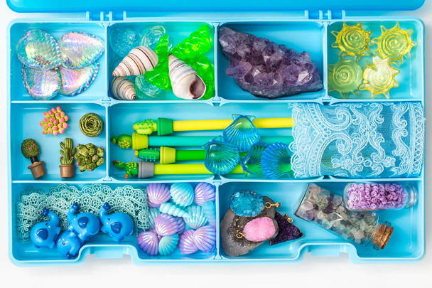 Container with cute toy items such as shells, pens, plastic succulents, crystals and stones, cartoon elephants, lace, top view - Photo, Image