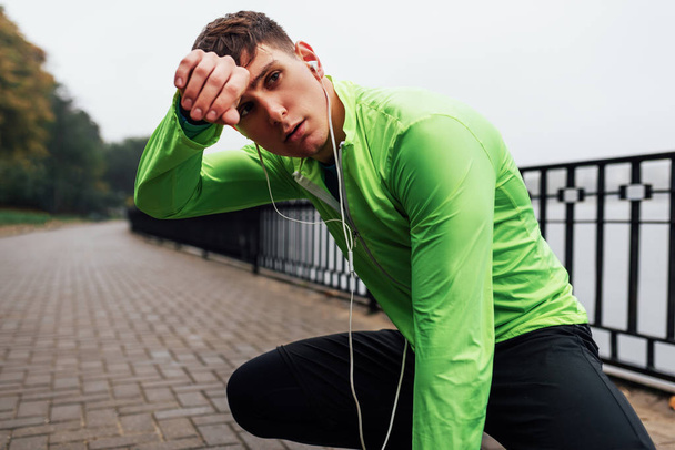 Horizontal image of athletic man stretching outdoor in the morning on the fog nature background. Fitness male exercising in the park and listenting the music on earphones. People and sport - Foto, Imagem