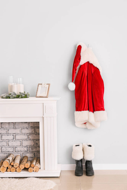 Kerstman kostuum opknoping op de muur in de buurt van open haard in de kamer - Foto, afbeelding