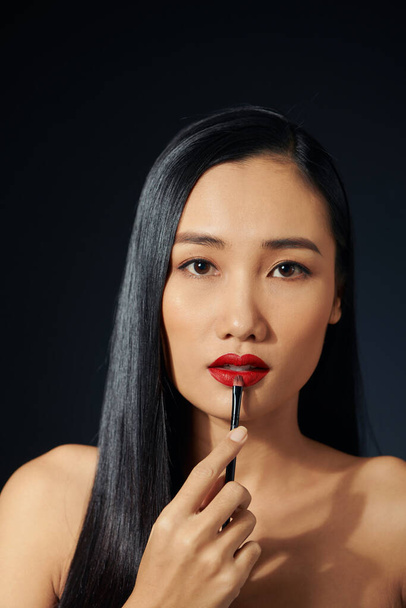 Beautiful woman paints lips with lipstick. Beautiful woman face. Makeup detail. Beauty girl with perfect skin. Red lips and nails manicure - Foto, Imagem