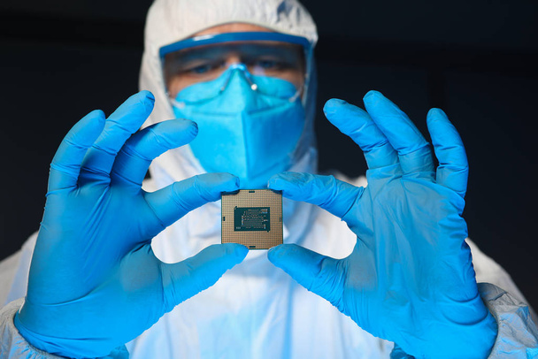 Человек в специальной униформе показывает микропроцессорный чип
 - Фото, изображение