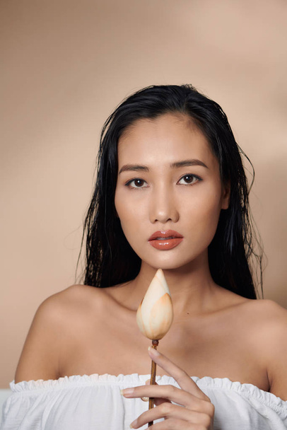 Fresh, natural skin. Attractive sensual woman with tan skin, holding dried lotus buds isolated on beige background - Fotoğraf, Görsel